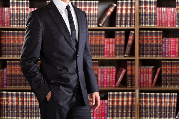 Midsection of lawyer with hand in pocket against books in shelves