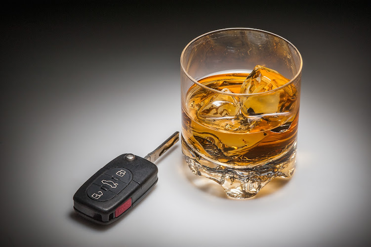 A set of car keys in the foreground and glass of whiskey behind.